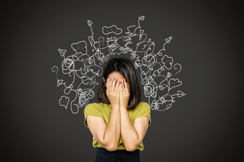 Photo of a woman covering her face with illustrations of many chaotic thoughts drawn around her head. 